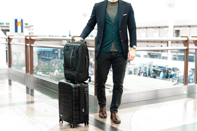 Dressed in a blue suit jacket and black pants man standing next to the black bag
